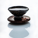 Tea Passion_Sven-Christian Lange_Branding Photography_Beautiful Antique Black Korean Pottery Art Bowl On Wooden Coaster With Little Tempelflowers_On White Reflecting Surface_Green Tea__Tea Ceremony