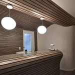 Arztpraxis-Design Empfangs-Tresen in der Chiropractic West von Chiropractor Corinna Haack im ästhetischen Spa Design mit geschwungenen Wänden und geschwungenen Möbeln und Produkt-Design mit dunklen Holz-Lamellen zum Wohlbefinden der Kunden