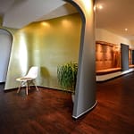 repräsentativer Empfangsbereich und Empfangs-Tresen aus Corian weiß geschwungene organisch geformte Wände Wartezimmer in lava-grau und innen goldfarben und Wartebereich mit großer brauner Leder Sitzfläche und gesteppter Leder Rückwand und Garderobe Praxis-Design in der Praxis für Dermatologie Venerologie und TCM Dr. med. May Sian Oei Schillerstr. 44b Ottensen im ästhetischen und zeitlosen Design von Lange Architekten