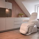 repräsentatives Behandlungszimmer mit Behandlungsstuhl und Einbaumöbeln in weiß und goldfarbenen Akzenten und roséfarbener Tapete Insignia von Arte Praxis-Design in der Praxis für Ästhetische Medizin Dr. med. Eveline Urselmann Milchstrasse 26 bis 28 Hamburg Pöseldorf Rotherbaum im ästhetischen und zeitlosen Design von Lange Architekten