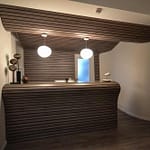 Arztpraxis-Design Empfangs-Tresen in der Chiropractic West von Chiropractor Corinna Haack im ästhetischen Spa Design mit geschwungenen Wänden und geschwungenen Möbeln und Produkt-Design mit dunklen Holz-Lamellen zum Wohlbefinden der Kunden