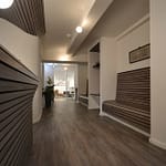 Arztpraxis-Design Empfangsbereich und Wartezone mit Blick auf den offenen Behandlungsraum in der Chiropractic West von Chiropractor Corinna Haack im ästhetischen Spa Design mit geschwungenen Wänden und geschwungenen Möbeln und Produkt-Design mit dunklen Holz-Lamellen zum Wohlbefinden der Kunden
