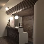 Arztpraxis-Design Empfangsbereich und Tresen in der Chiropractic West von Chiropractor Corinna Haack im ästhetischen Spa Design mit geschwungenen Wänden und geschwungenen Möbeln und Produkt-Design mit dunklen Holz-Lamellen zum Wohlbefinden der Kunden