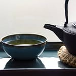 Tea_Passion_Sven-Christian Lange_Branding Photography_Ancient Black Cast Iron Kettle On Coaster Made Of Bast With Drop On Spout And Steaming Turquoise Tea Bowl On Platter