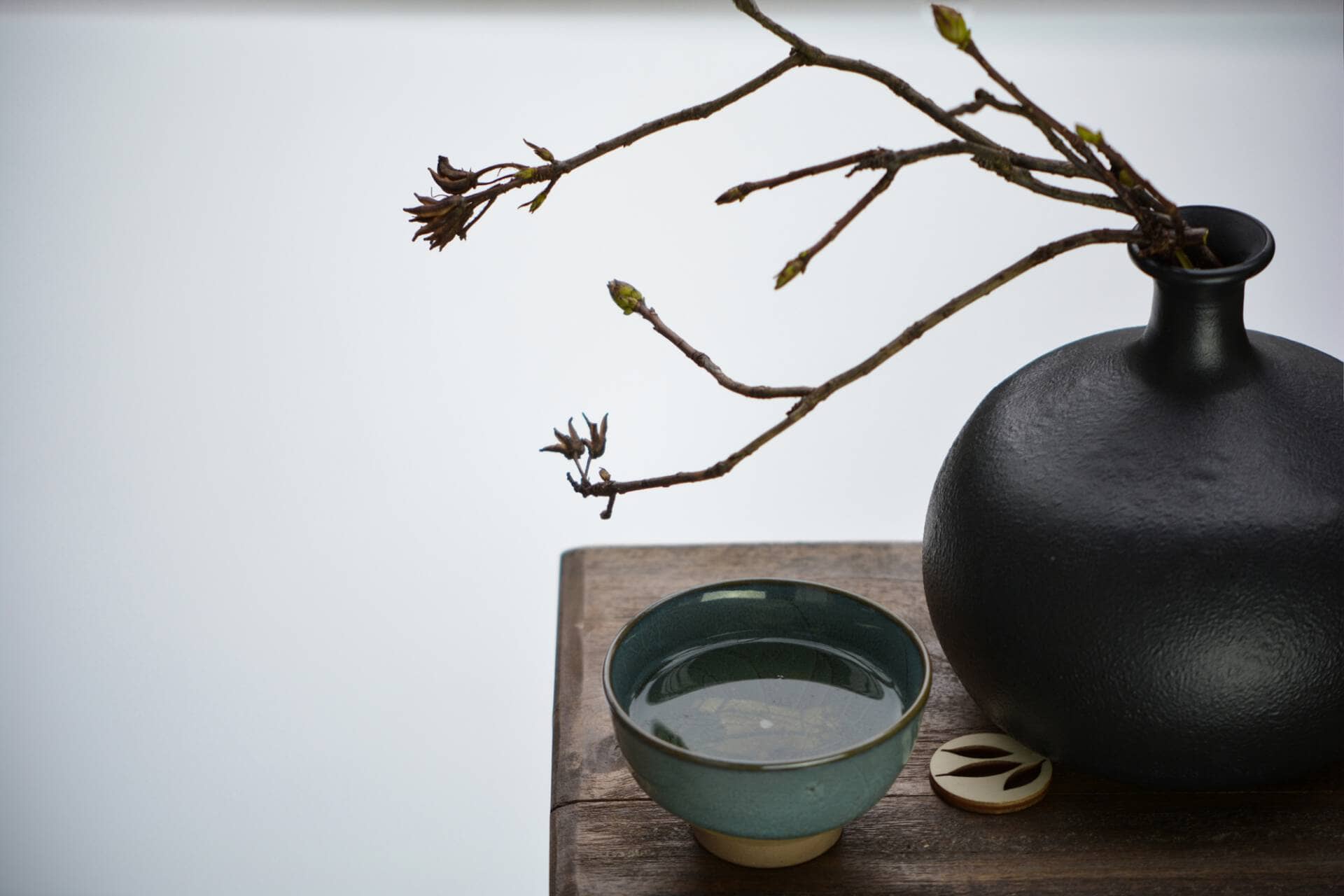 Tea Passion_Sven-Christian Lange_Branding Photography_Black Cast Iron Vase And Branch With Buds With Turquoise Matcha Bowl On Ancient Wooden Stand_Tea Ceremony_Wabi Sabi